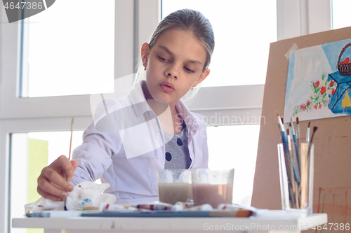 Image of Girl-artist concentrated wets brush in paint for drawing still life