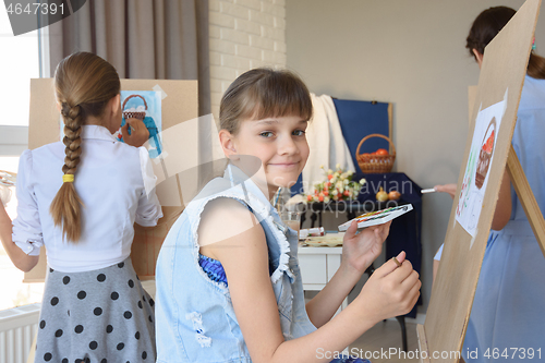 Image of Girl smiles sitting at easel with paints in the studio