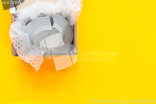 Image of On a yellow background lies an open package, a box with a broken plate
