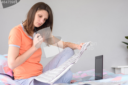 Image of A girl is looking for work looking through ads in the newspaper, next to a laptop