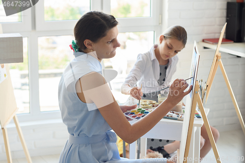 Image of Concentrated girl draws on easel next to a young girl