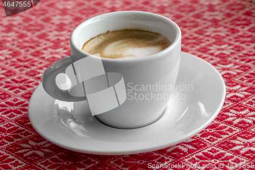 Image of White cup of coffee with foam and bubbles on a red tablecloth