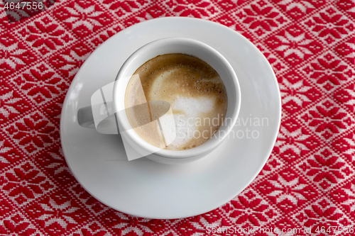 Image of White cup of coffee with foam and bubbles on a red tablecloth