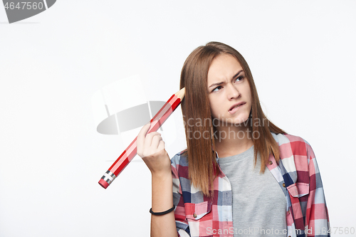 Image of Contemplating girl scratching her head with big pencil