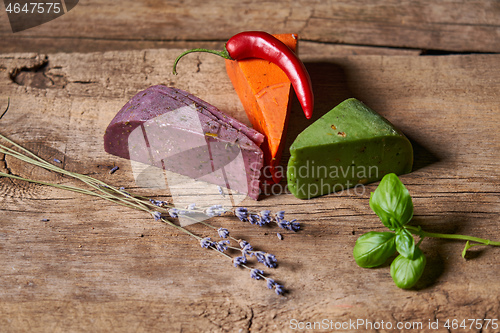 Image of Three different cheeses on rough wooden planks: lavender, paprika and pesto cheeses