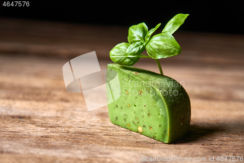 Image of A piece of gourmet basil cheese with twig of basil on rough wooden planks