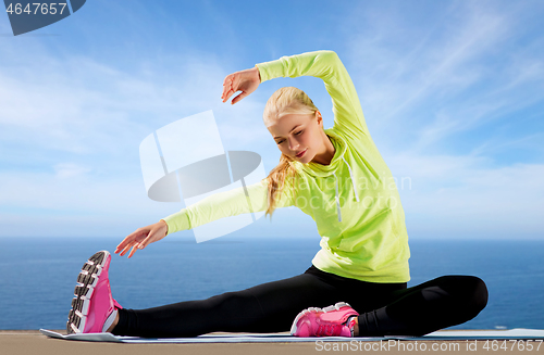 Image of woman stretching on exercise mat over sea