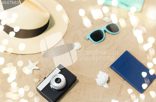 Image of camera, passport, sunglasses and hat on beach sand