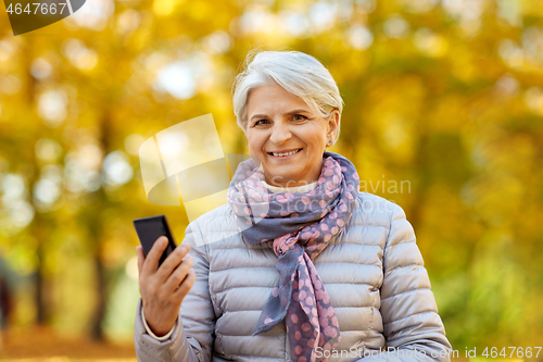 Image of happy senior woman with smartphone at autumn park