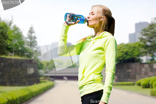 Image of woman drinking water after exercising in city park