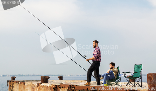 Image of male friends with fishing rods on sea pier