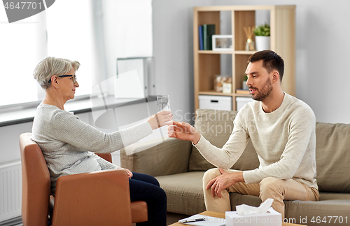 Image of senior psychologist giving water to man patient