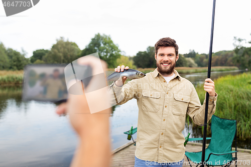 Image of friend photographing fisherman with fish at lake