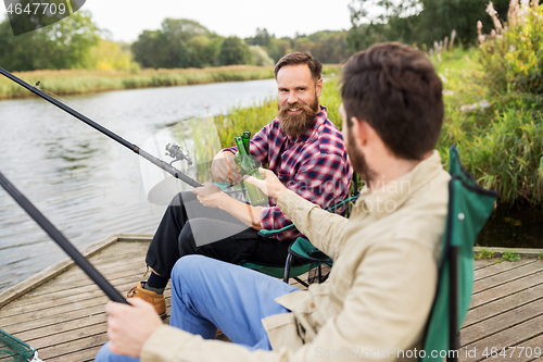 Image of happy friends fishing and drinking beer on pier