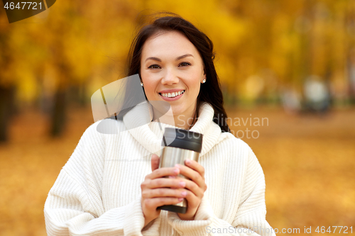 Image of woman with hot drink in tumbler at autumn park