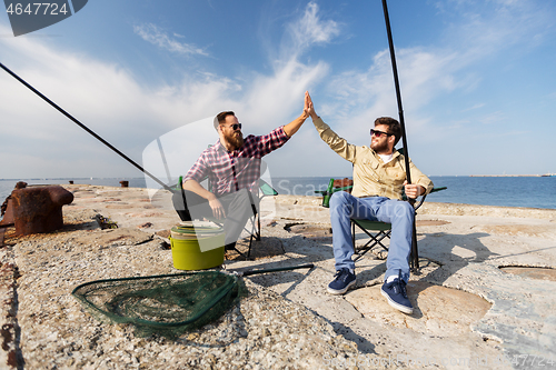 Image of male friends with fishing rods making high five