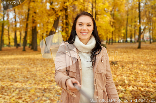 Image of woman taking picture by selfiestick at autumn park