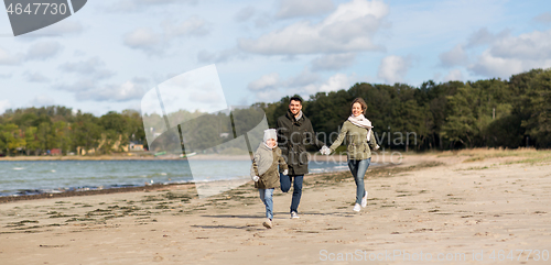 Image of happy family running along autumn beach