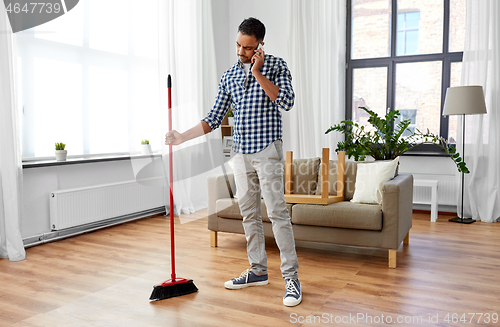 Image of man with broom cleaning and calling on smartphone