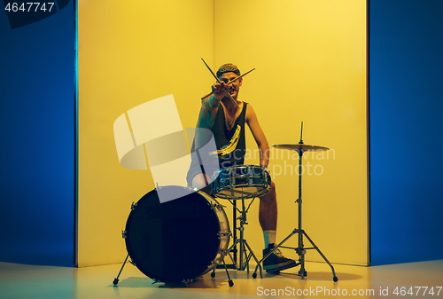 Image of Young caucasian musician inspired performing on yellow background in neon light