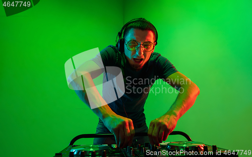 Image of Young caucasian musician in headphones performing on green background in neon light