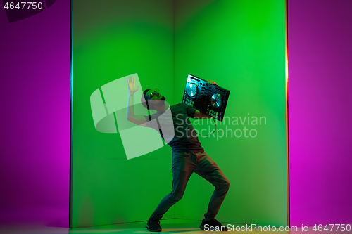 Image of Young caucasian musician in headphones performing on bicolored green-purple background in neon light