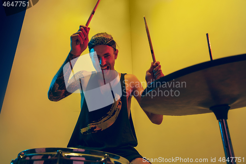 Image of Young caucasian musician inspired performing on yellow background in neon light