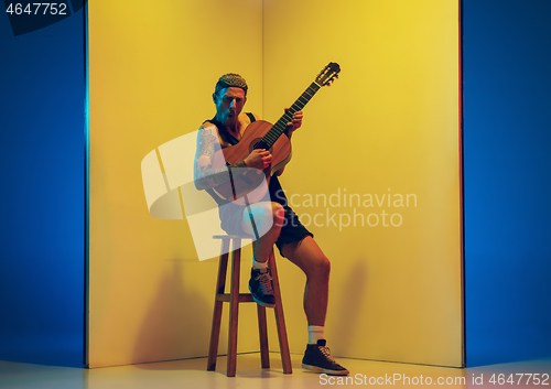 Image of Young caucasian musician inspired performing on yellow background in neon light