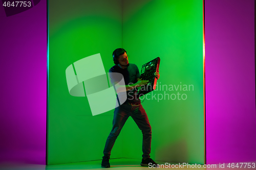 Image of Young caucasian musician in headphones performing on bicolored green-purple background in neon light