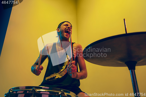 Image of Young caucasian musician inspired performing on yellow background in neon light