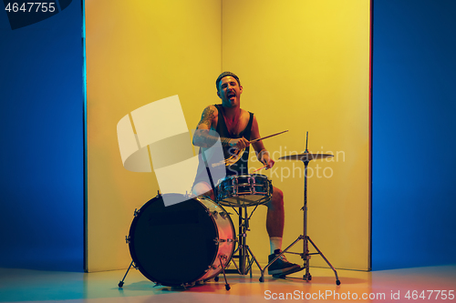 Image of Young caucasian musician inspired performing on yellow background in neon light