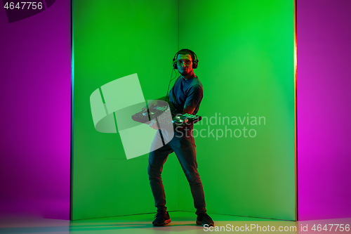 Image of Young caucasian musician in headphones performing on bicolored green-purple background in neon light