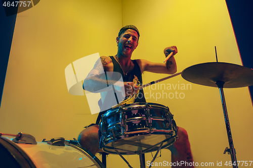 Image of Young caucasian musician inspired performing on yellow background in neon light