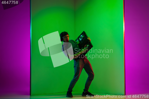 Image of Young caucasian musician in headphones performing on bicolored green-purple background in neon light