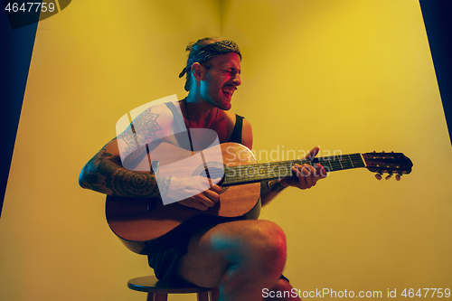 Image of Young caucasian musician inspired performing on yellow background in neon light