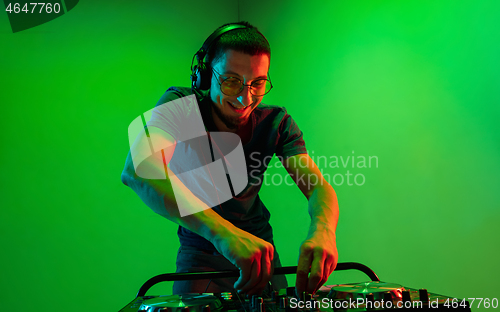 Image of Young caucasian musician in headphones performing on green background in neon light