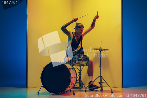 Image of Young caucasian musician inspired performing on yellow background in neon light