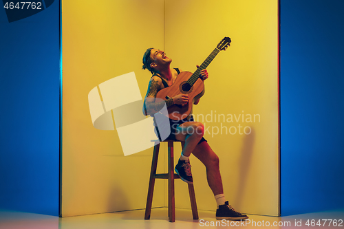 Image of Young caucasian musician inspired performing on yellow background in neon light