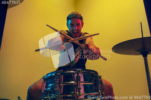 Image of Young caucasian musician inspired performing on yellow background in neon light