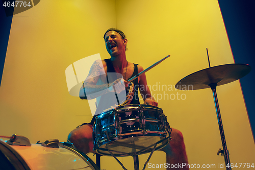 Image of Young caucasian musician inspired performing on yellow background in neon light