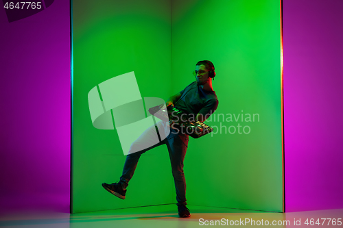 Image of Young caucasian musician in headphones performing on bicolored green-purple background in neon light