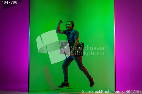 Image of Young caucasian musician in headphones performing on bicolored green-purple background in neon light