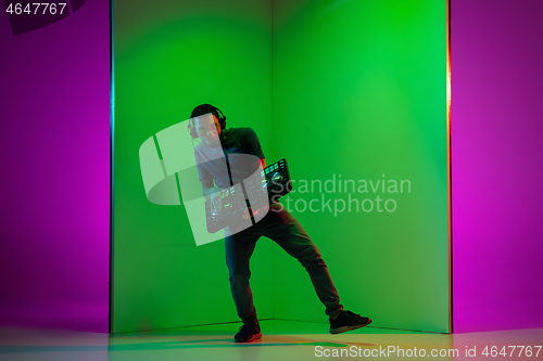 Image of Young caucasian musician in headphones performing on bicolored green-purple background in neon light