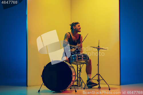 Image of Young caucasian musician inspired performing on yellow background in neon light