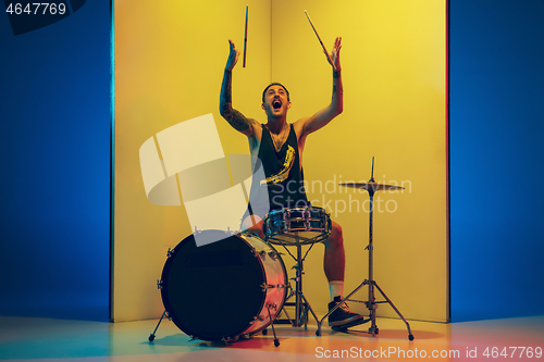 Image of Young caucasian musician inspired performing on yellow background in neon light