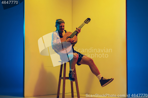 Image of Young caucasian musician inspired performing on yellow background in neon light