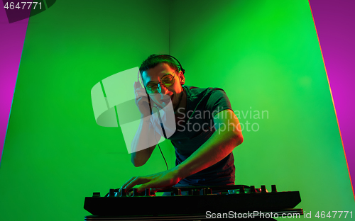 Image of Young caucasian musician in headphones performing on bicolored green-purple background in neon light