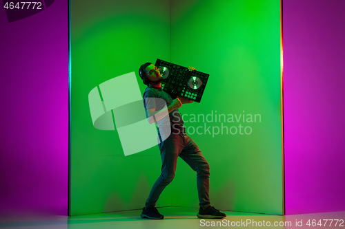 Image of Young caucasian musician in headphones performing on bicolored green-purple background in neon light