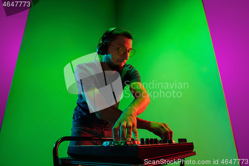 Image of Young caucasian musician in headphones performing on bicolored green-purple background in neon light