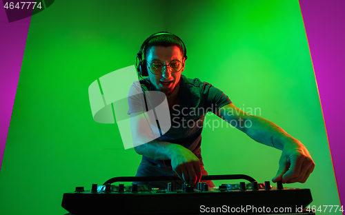 Image of Young caucasian musician in headphones performing on bicolored green-purple background in neon light